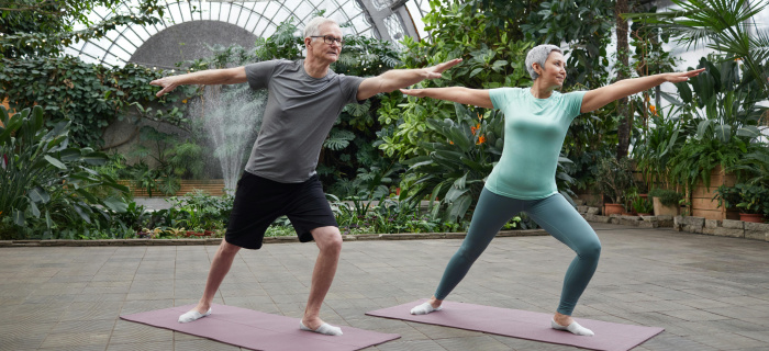Un homme et une femme aux cheveux gris font de l'exercice sur des tapis de de yoga dans une serre de jardin botanique