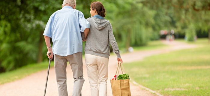 Une femme porte un sac de courses et accompagne un homme plus âgé avec une canne