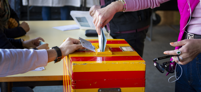 Personne glissant son enveloppe de vote dans une urne rouge et jaune. Photo chancellerie