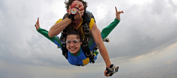 Un non-voyant saute en parachute accroché sur le dos de son instructeur, les deux sourient et le non-voyant se masque les yeux.