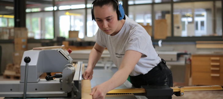 Amélie Christie, 20 ans, apprentie charpentière, coupe un morceau de bois avec une machine spécialisée