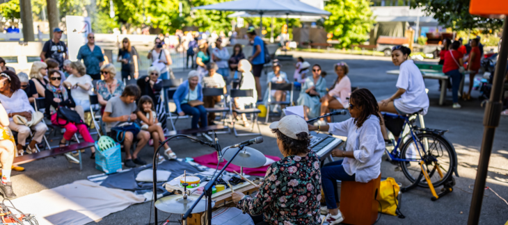Des personnes de diverses générations sont réunies en plein air et écoutent un groupe de musique