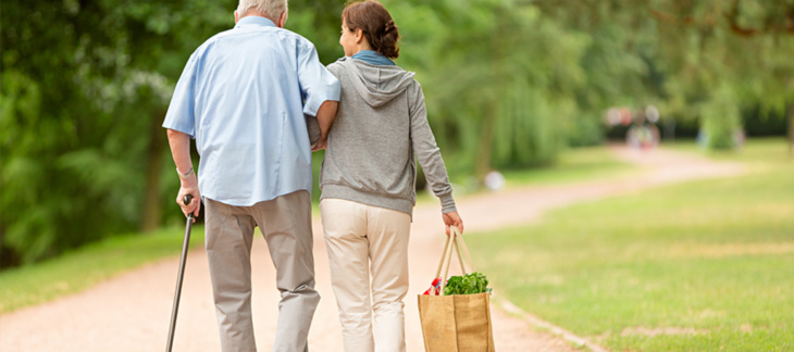 Une femme porte un sac de courses et accompagne un homme plus âgé avec une canne
