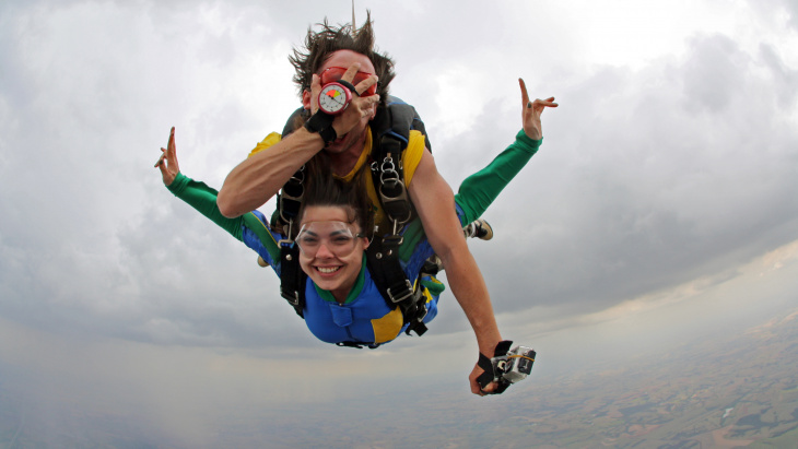 Un non-voyant saute en parachute accroché sur le dos de son instructeur, les deux sourient et le non-voyant se masque les yeux.