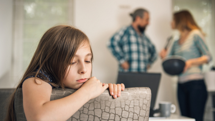 enfant accoudée avec sa famille qui se dispute en arrière-plan