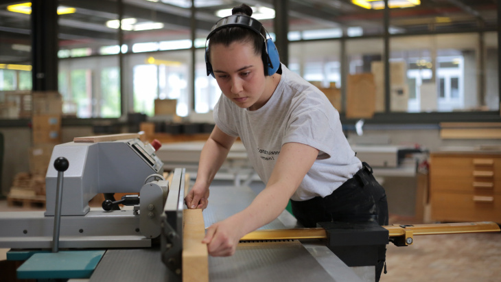 Amélie Christie, 20 ans, apprentie charpentière, coupe un morceau de bois avec une machine spécialisée