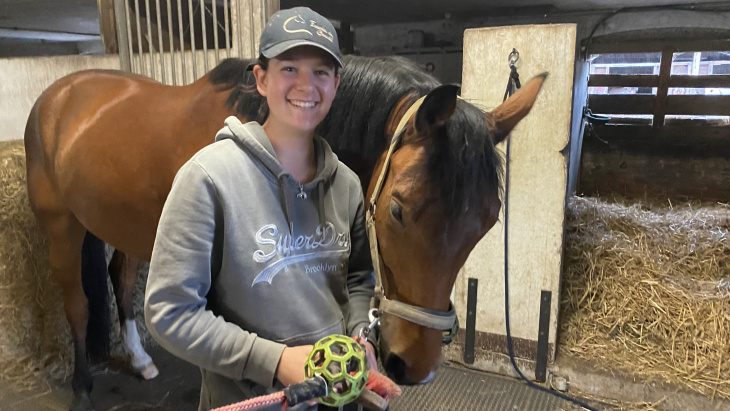 Alicia Rivolet, apprentie gardienne de chevaux, en compagnie d'un cheval devant un box