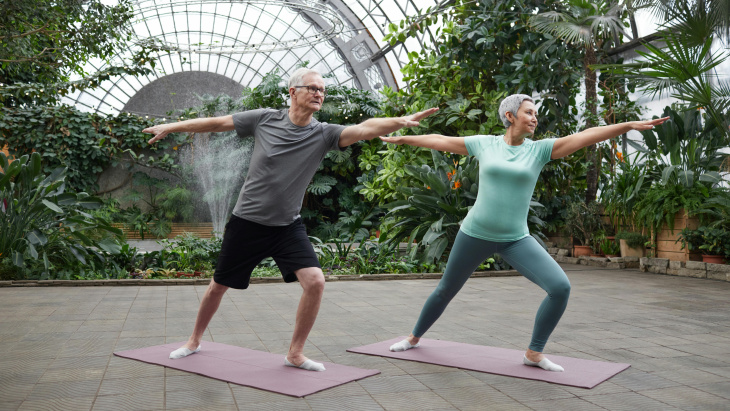 Un homme et une femme aux cheveux gris font de l'exercice sur des tapis de de yoga dans une serre de jardin botanique