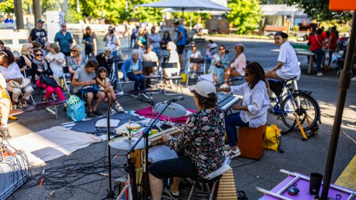 Des personnes de diverses générations sont réunies en plein air et écoutent un groupe de musique