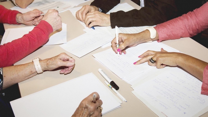 Des mains de plusieurs personnes remplissent des feuilles de notes © Plateforme seniors